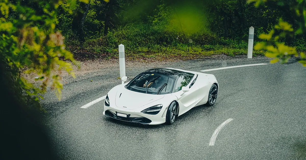 A white Mclaren 720S turns into a sharp corner on a wet road in a forest