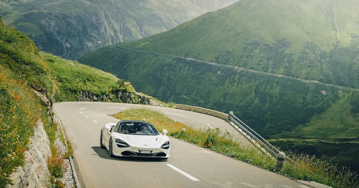 A white McLaren 720S exits a hairpin corner on an alpine pass during an Ultimate Driving Tours experience.