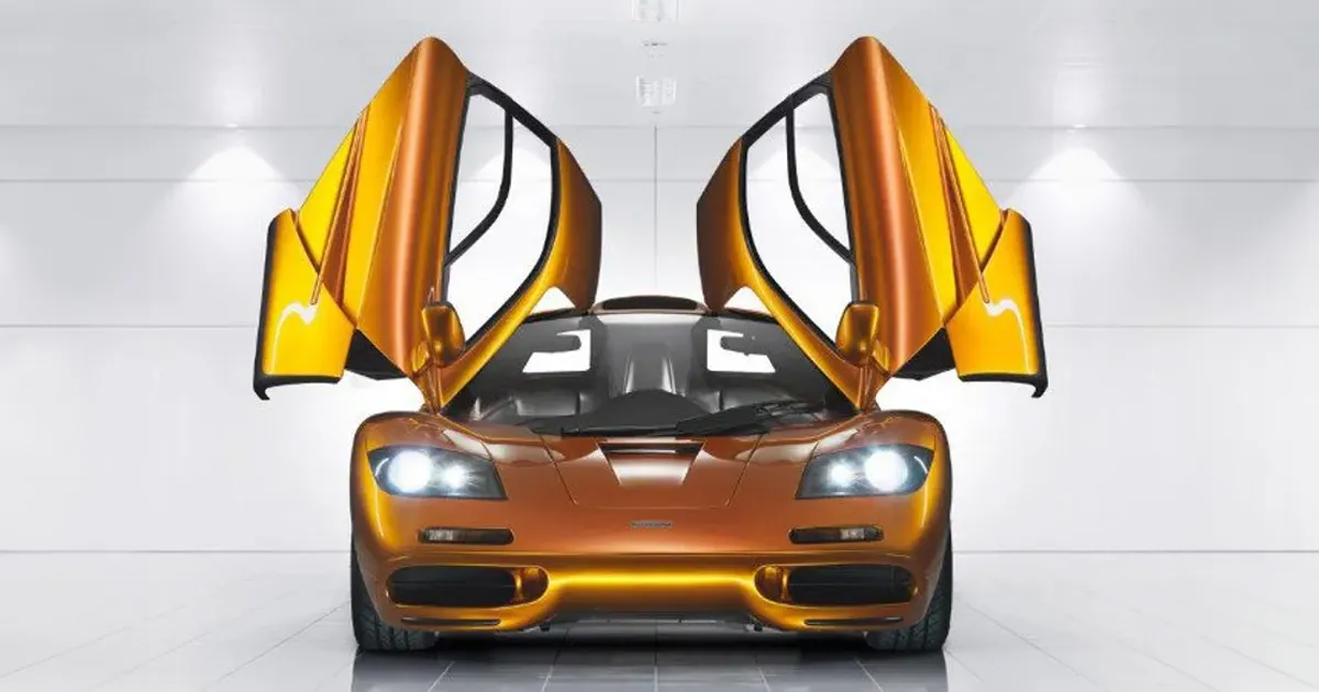 A metallic orange McLaren F1 with its dihedral doors open to the sky and its headlights on