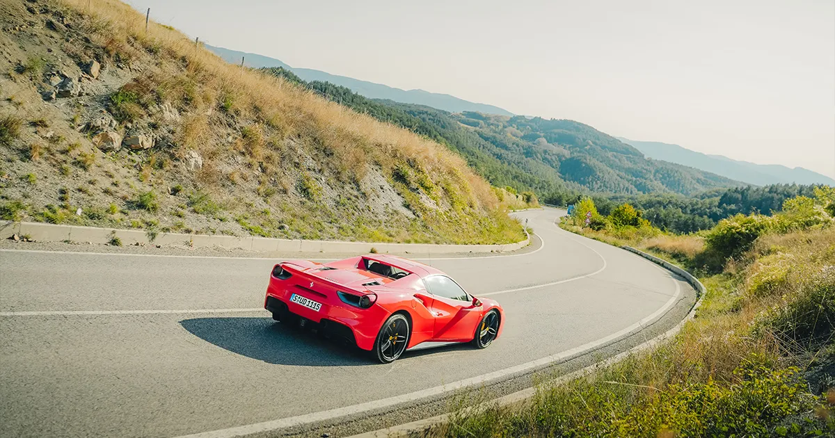 A red Ferrari 488 rounds a sweeping corner in the countryside