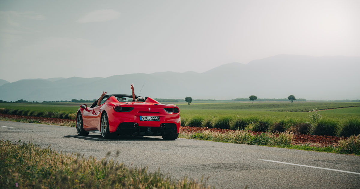 Driver and passenger of a red Ferrari with hands aloft