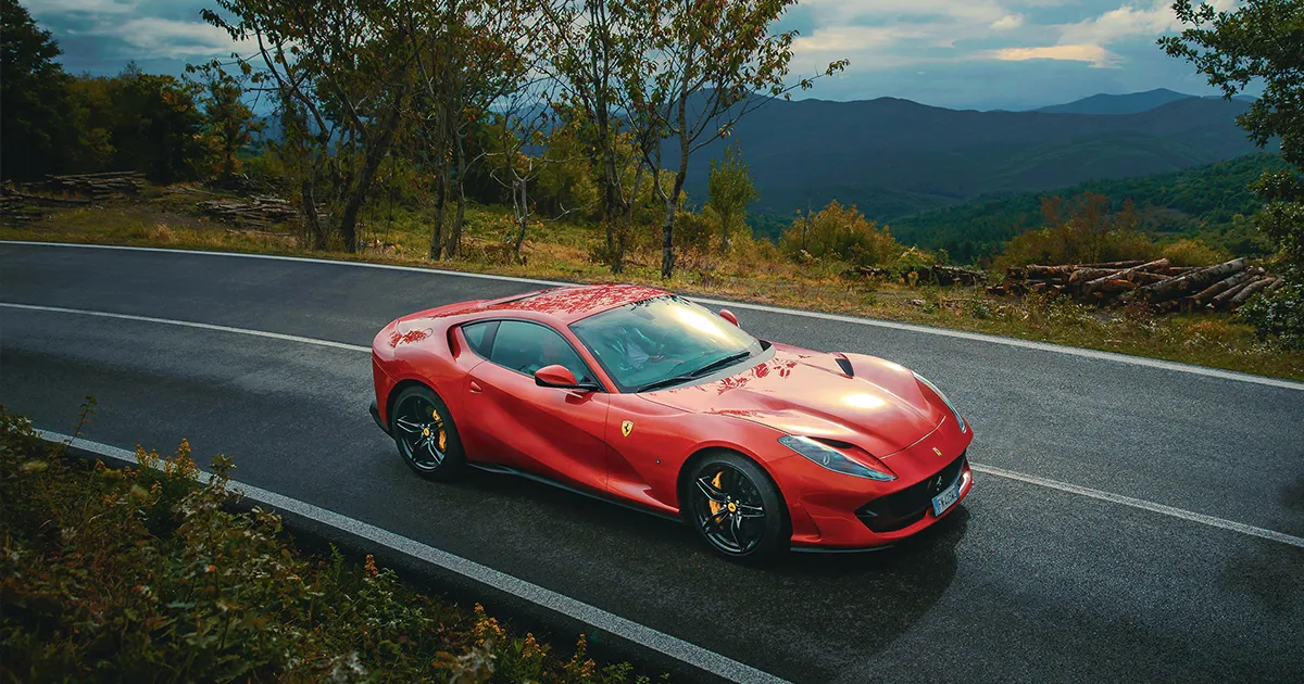 A red Ferrari 812 Superfast rounds a corner on a high country road.
