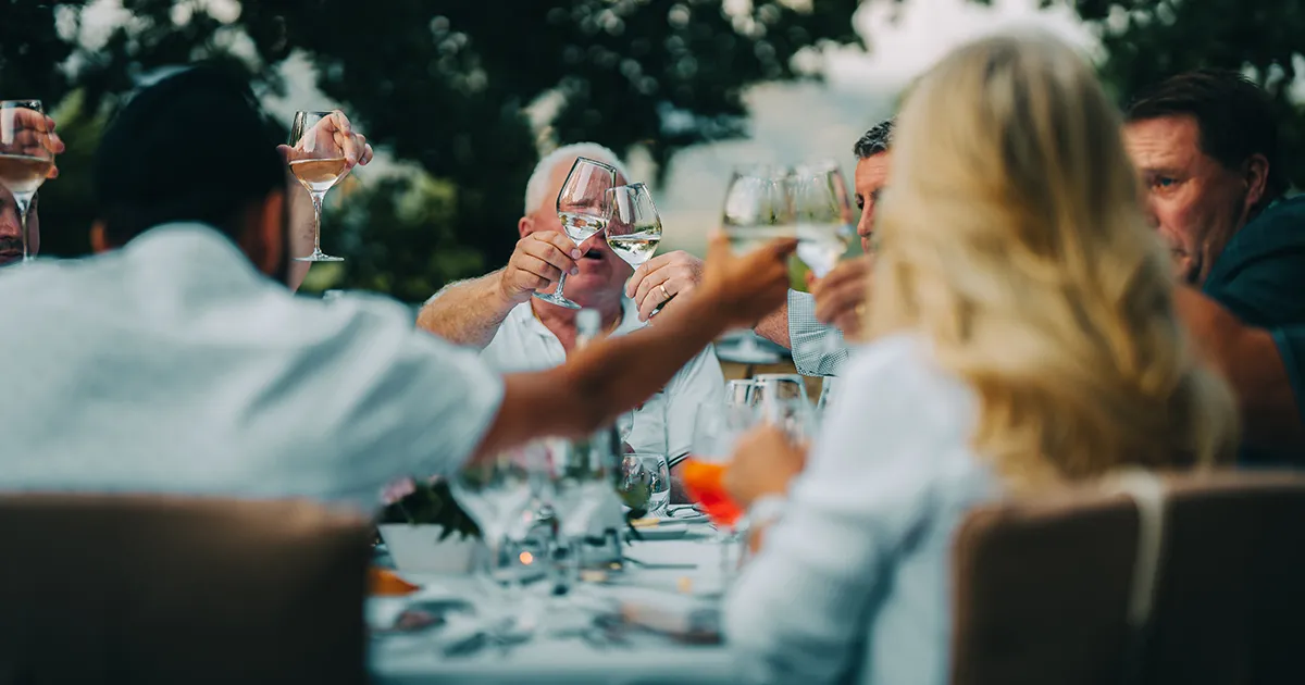 Happy guests toast wine glasses around a dinner table.