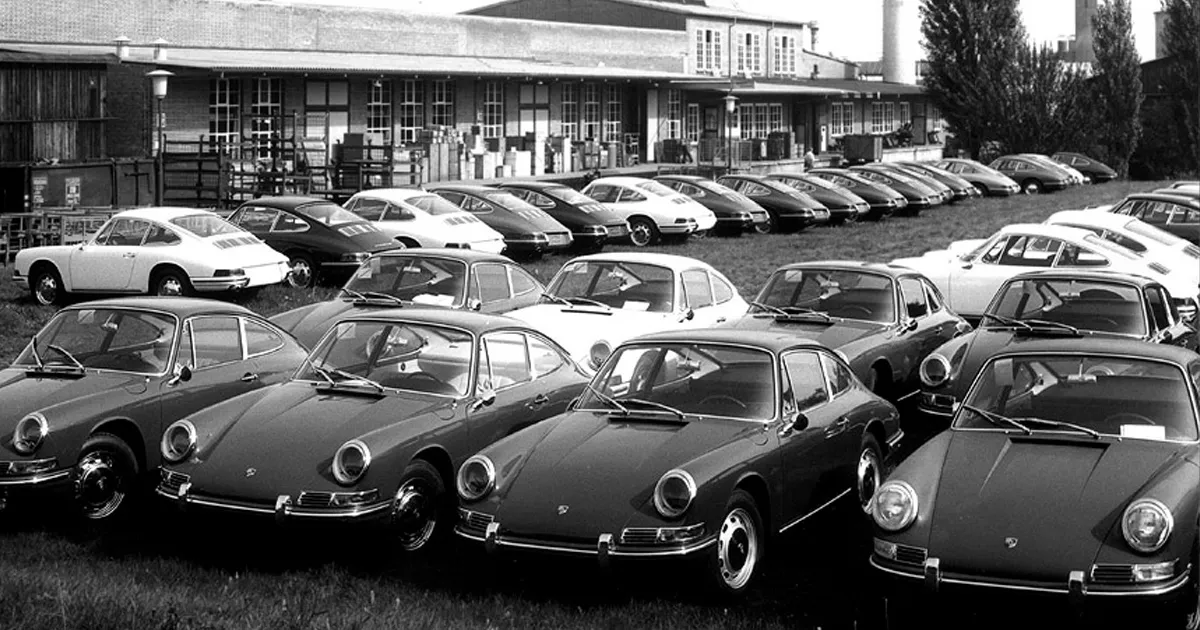 A fleet of early Porsche 911s sitting in lines on a factory lot.