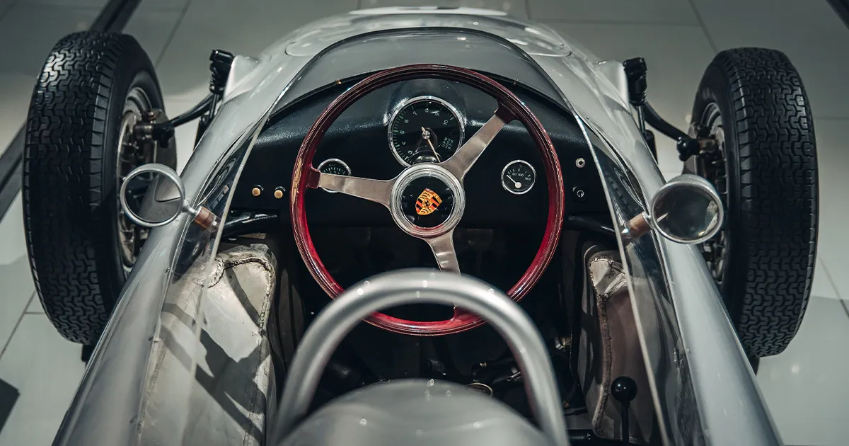 The sparse interior and steering wheel of a vintage silver Porsche racing car.