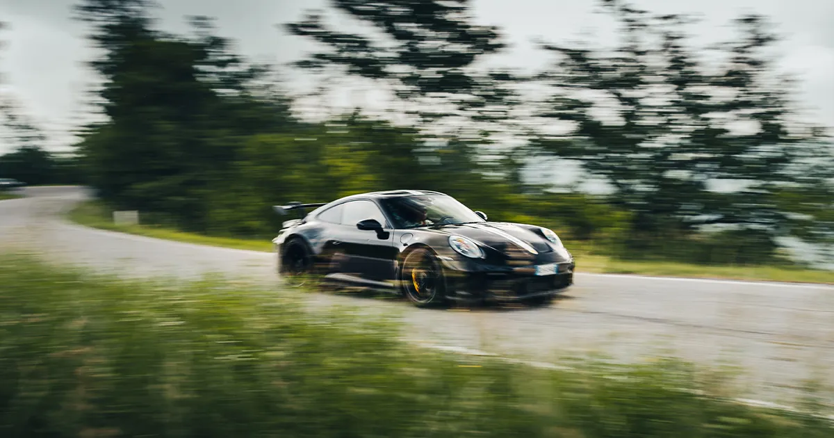 A black late model Porsche 911 tackles a sweeping corner at pace.