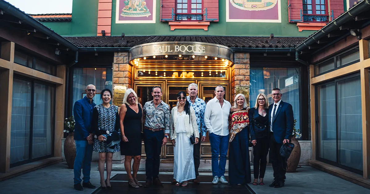 A small group of Ultimate Driving Tours guests standing happily outside the entrance to Restaurant Paul Bocuse.