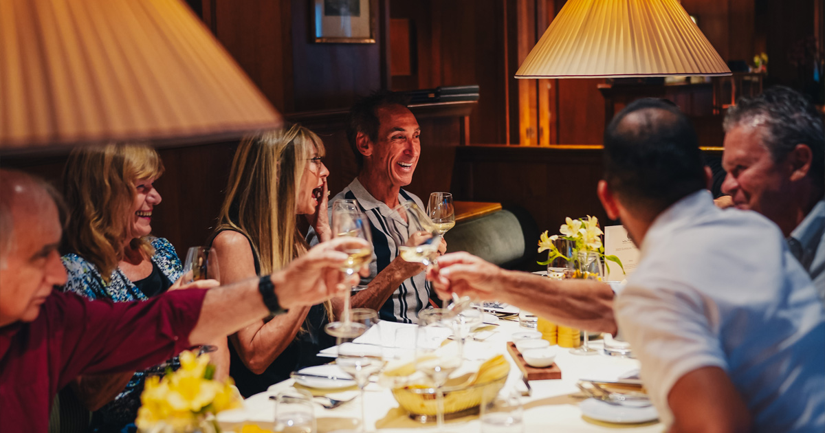 A group of guests share happy conversation around the dining table during an Ultimate Driving Tours experience.