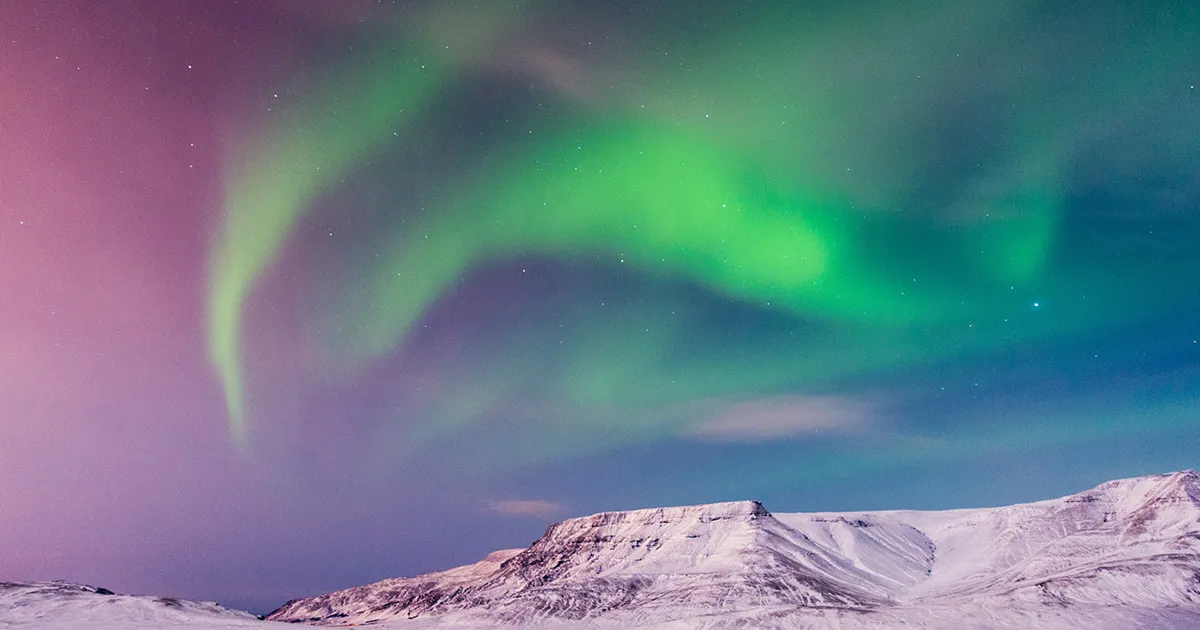 The northern lights light up the sky above snowcapped mountains. 