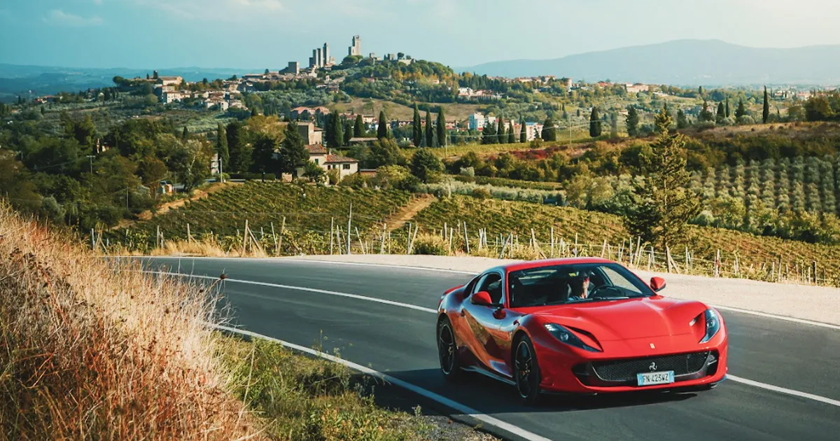 A red Ferrari rounds a vine-covered corner in Tuscany on an Ultimate Driving Tours luxury adventure.
