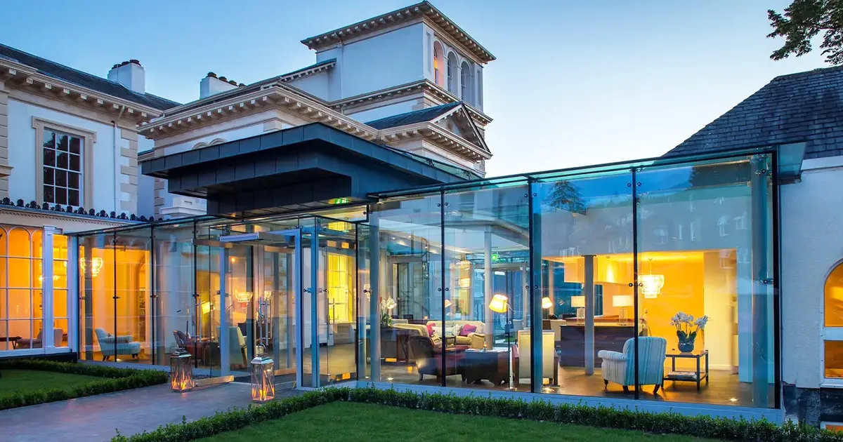 A glass-walled bar attached to an English country manor seen in the evening.