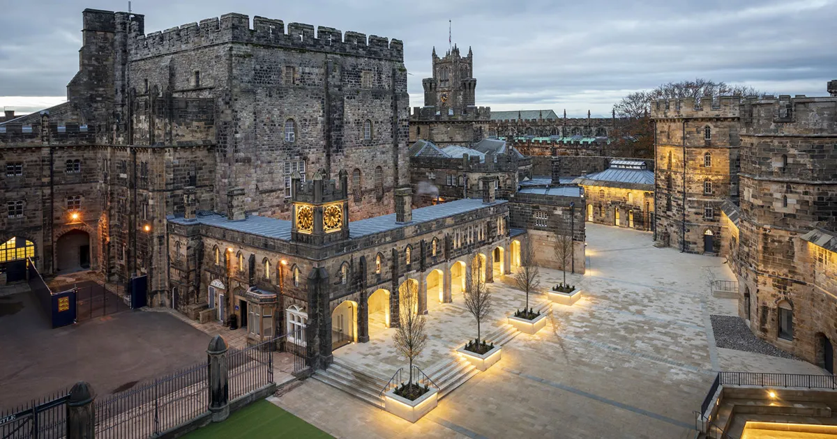 A huge stone castle in northern England is illuminated in the evening.