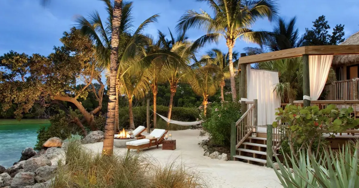 A private beach villa on a small island in the Florida Keys with sun loungers and deck surrounded by palm trees, Little Palm Island.