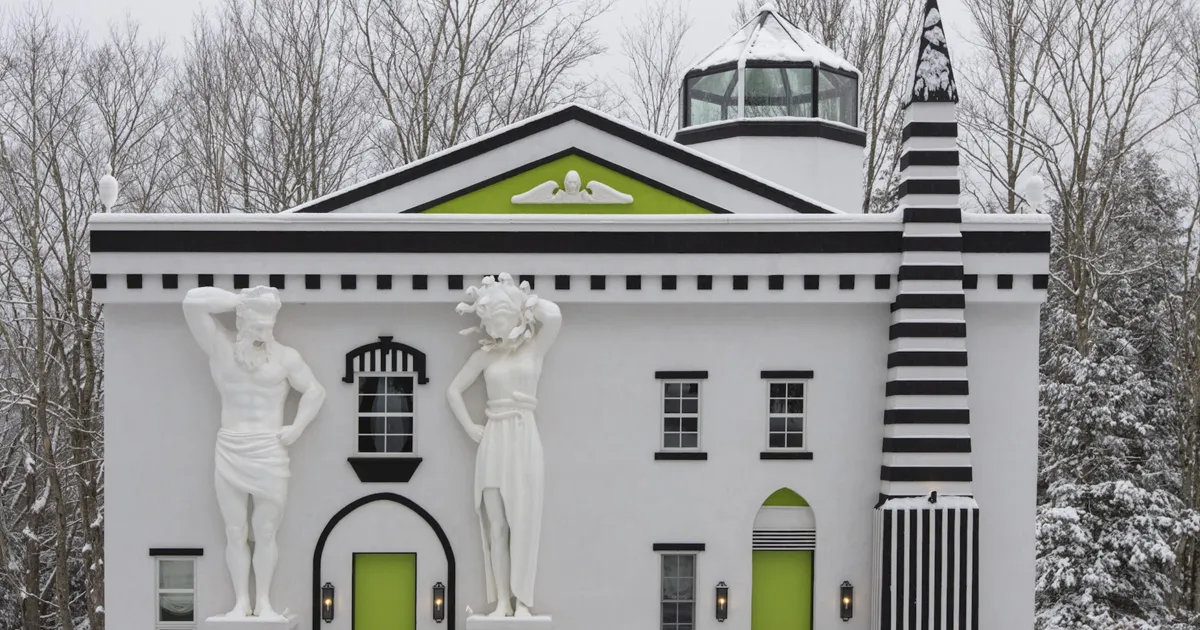 The exterior of a square white building with black trim, lime green doors and large marble statues, The Roxbury hotel, Catskills.