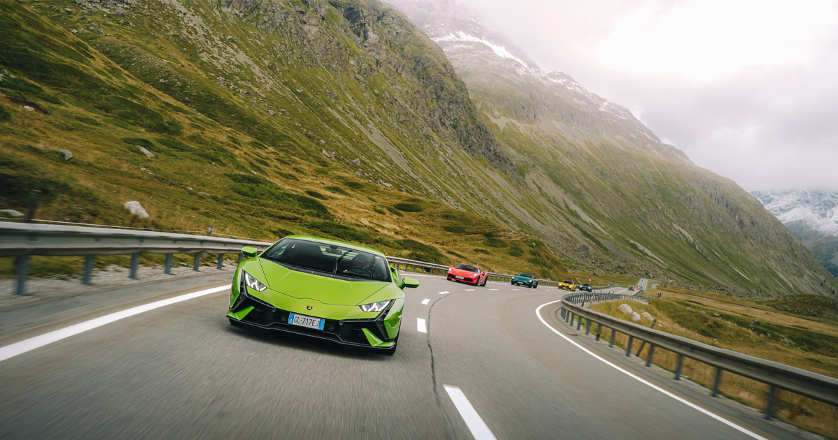 A green Lamborghini Huracan leads a convoy of supercars through the mountains in Europe