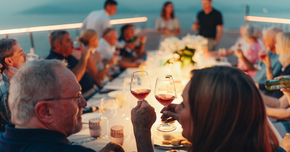 A couple toast wine glasses at the head of a long al fresco dinner table