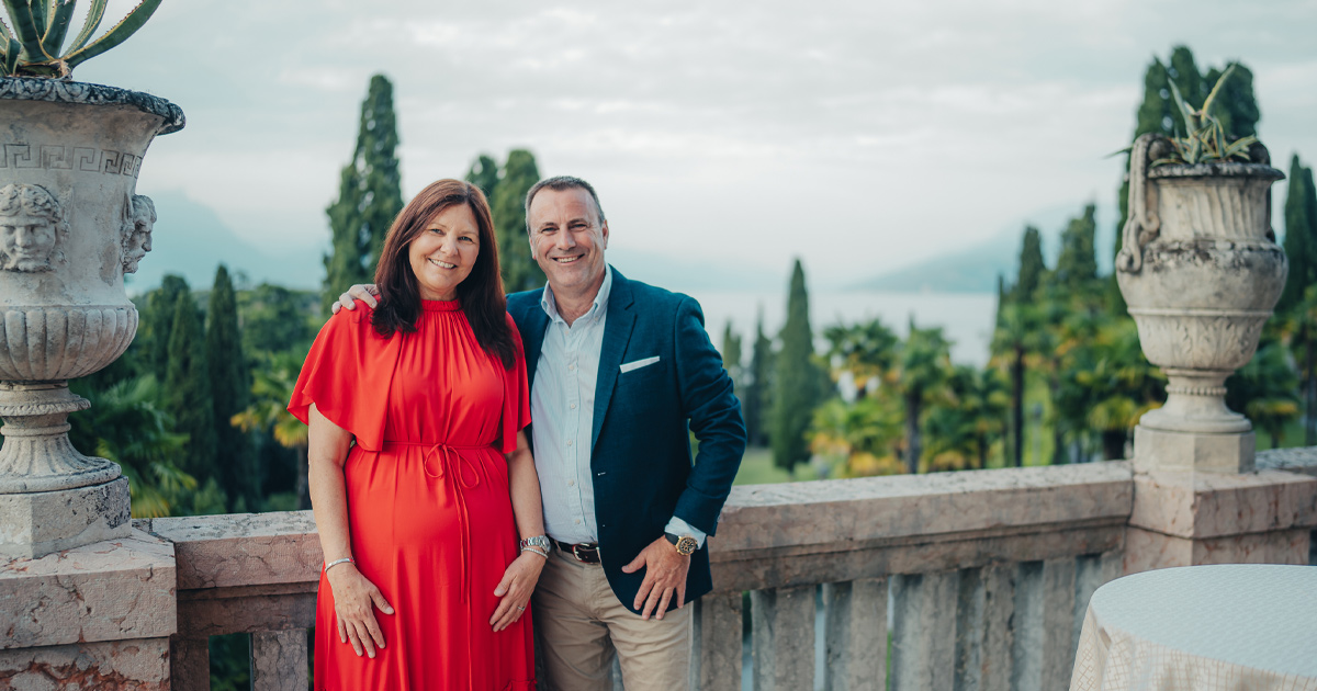 A happy couple in smart casual dress pose on an elegant stone balcony
