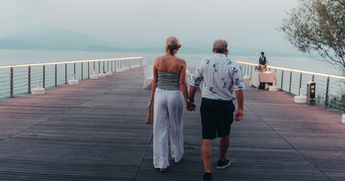 A couple walk on a stylish timber pier as a waiter awaits them at a private dinner table