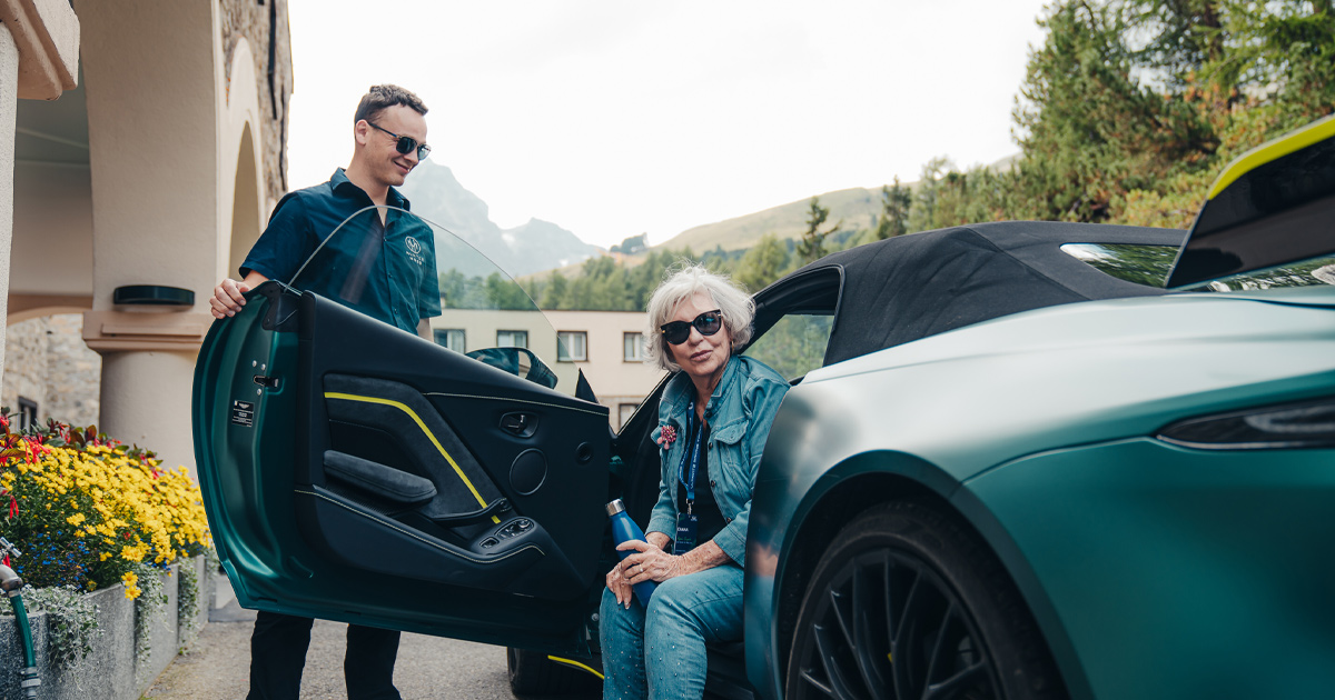 A man assists a lady as she exits a green Aston Martin Vantage