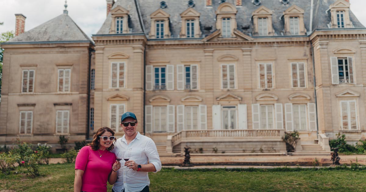 A happy couple pose in front of an elegant historic mansion in Europe