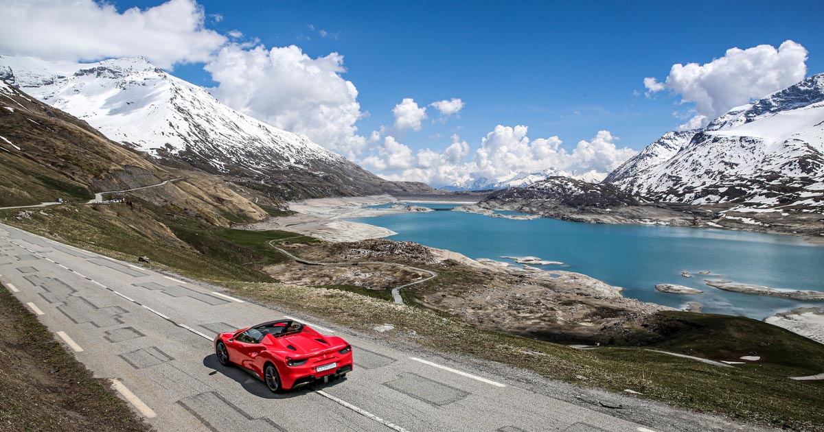 A red Ferrari 488 Spyder cruising alongside a beautiful alpine lake in Switzerland