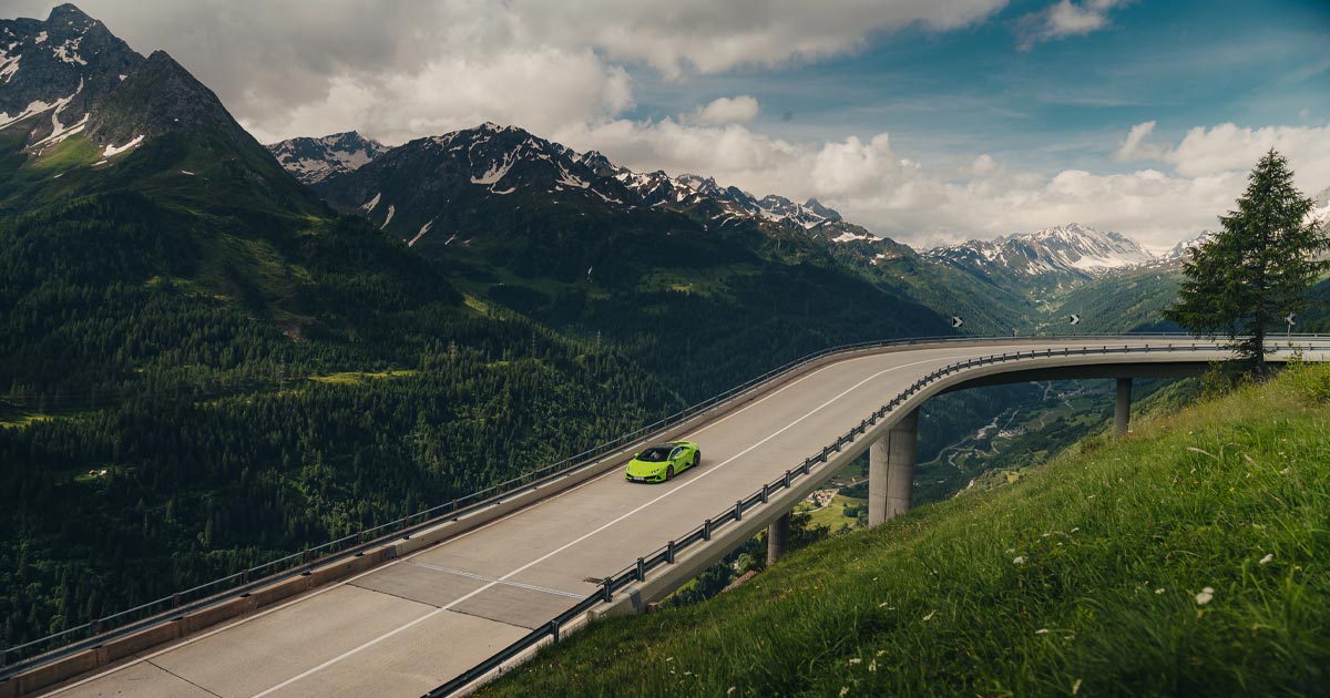 A green Lamborghini Huracan cruising on a bridge road high in the European Alps.