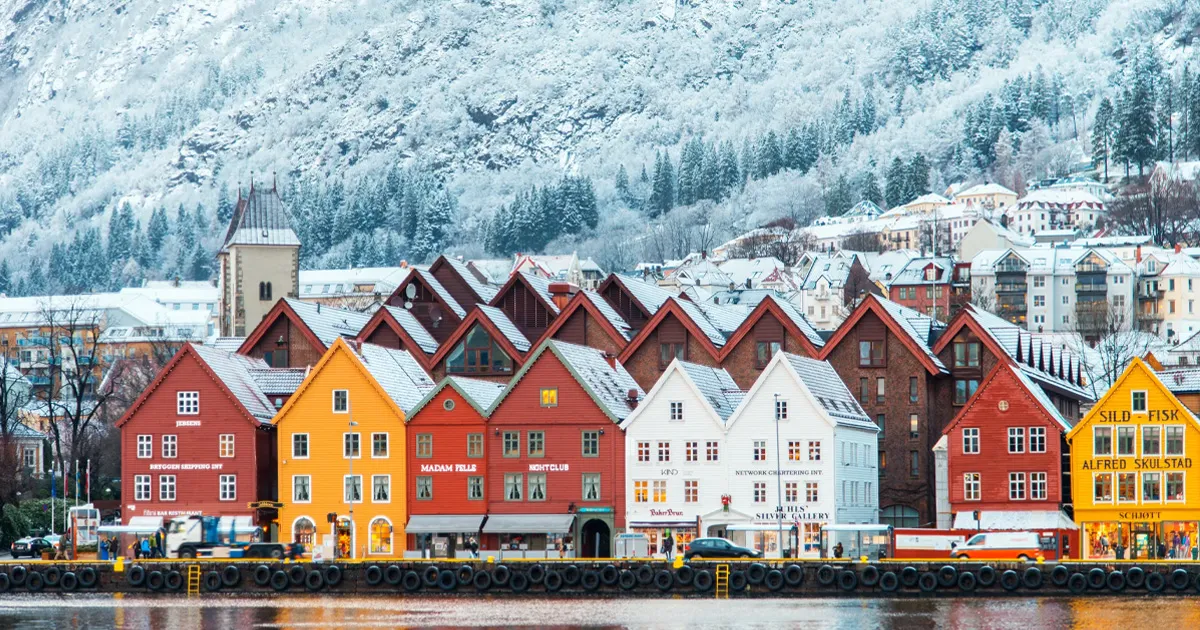 A row of brightly coloured buildings reflected in a lake at a snowy alpine resort