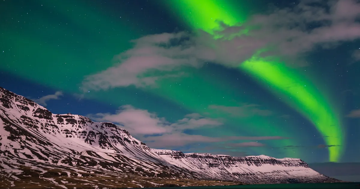 Vivid green patterns stretch across the sky above arctic mountains as the aurora borealis is seen from below.