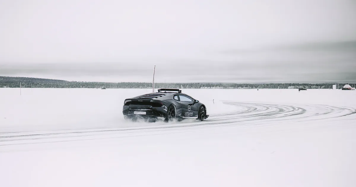 A black Lamborghini executes a controlled drift on a track on a frozen lake.