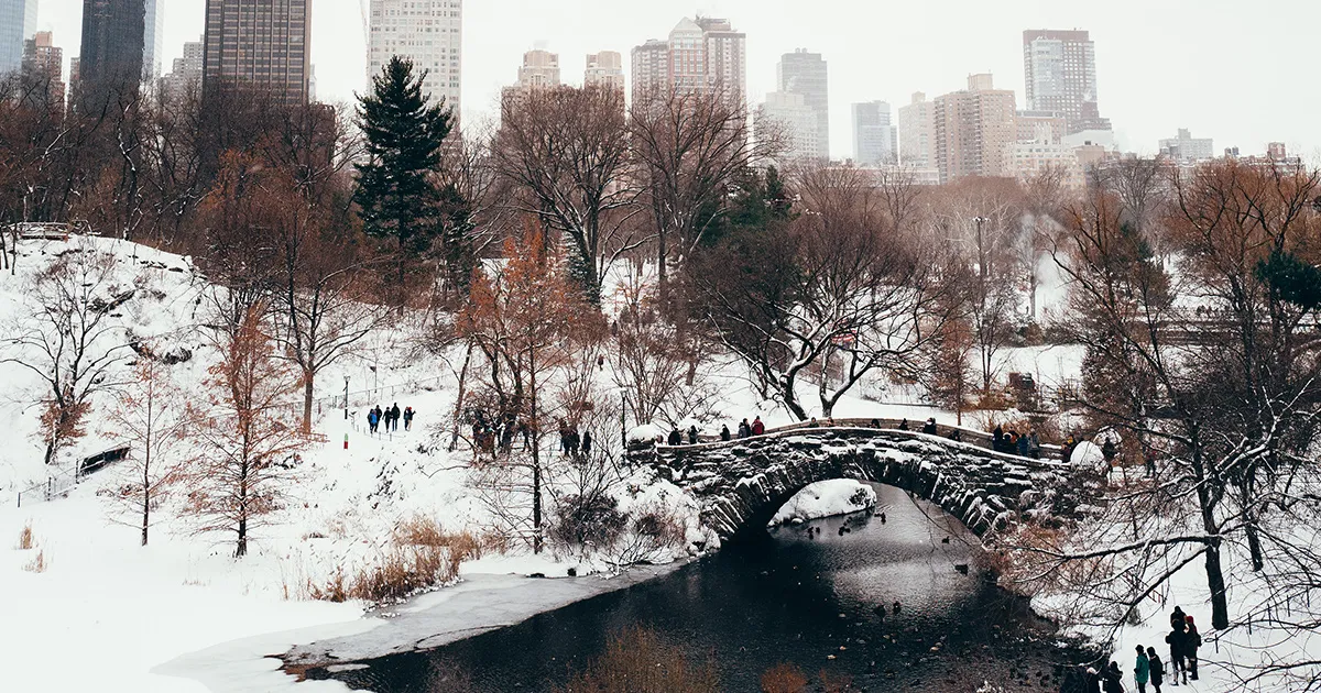 People walking across a small bridge crosses a river in snow-covered Central Park, New York.