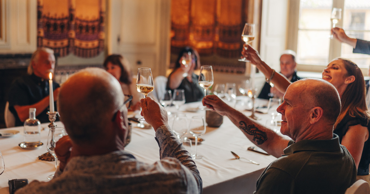 Luxury tour guests share a toast around a grand white-clothed table in France