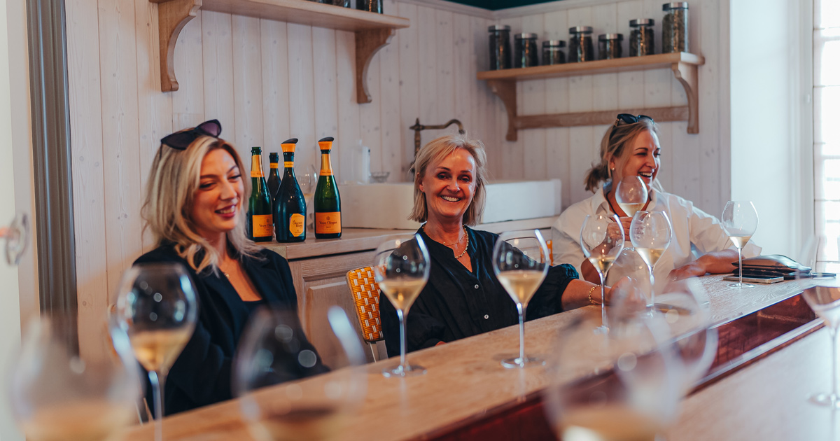 Three well-dressed ladies smile as they enjoy a Veuve Clicquot champagne tasting on a European tour