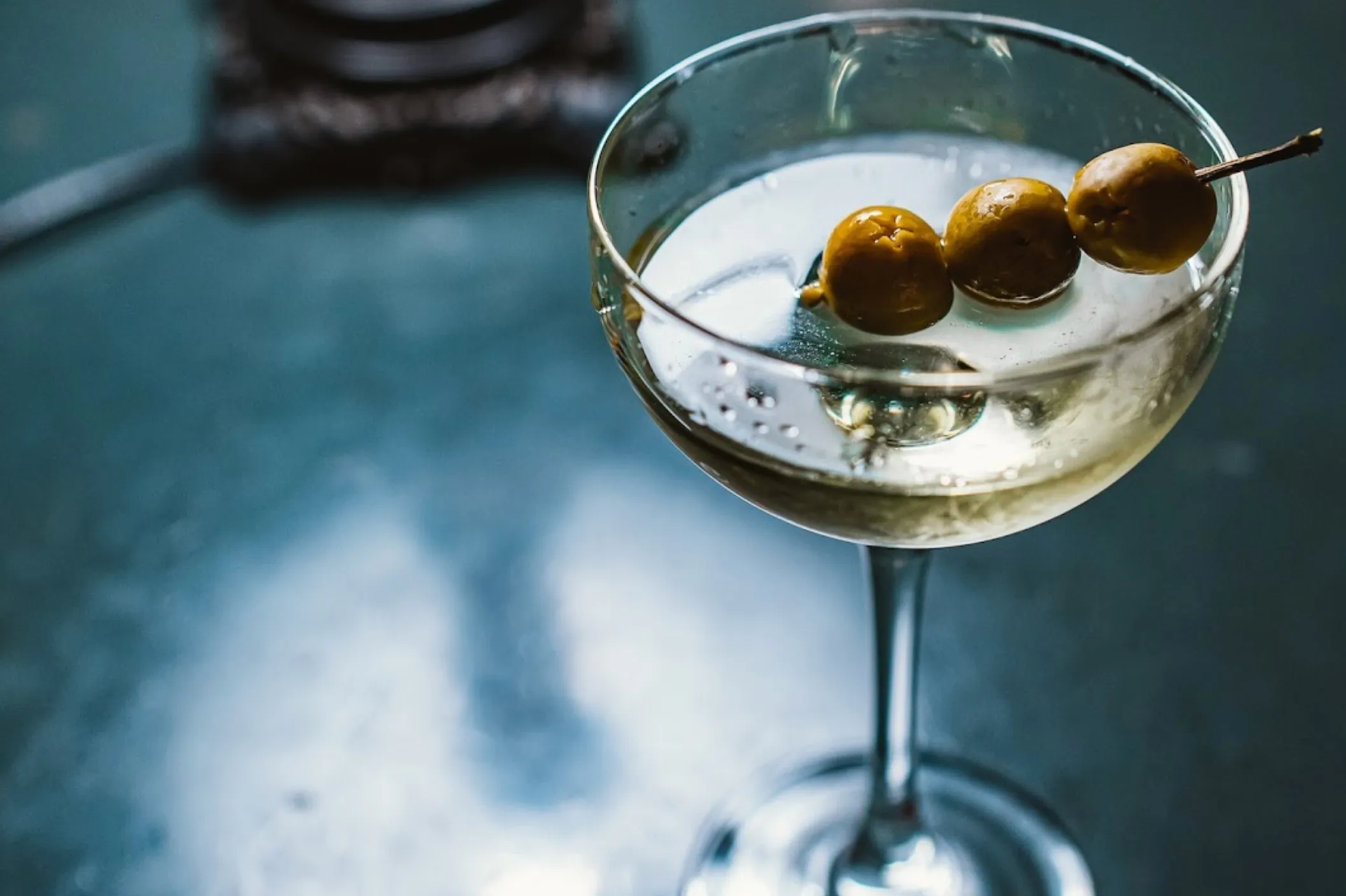 A martini glass holds a vodka martini with three olives on a skewer