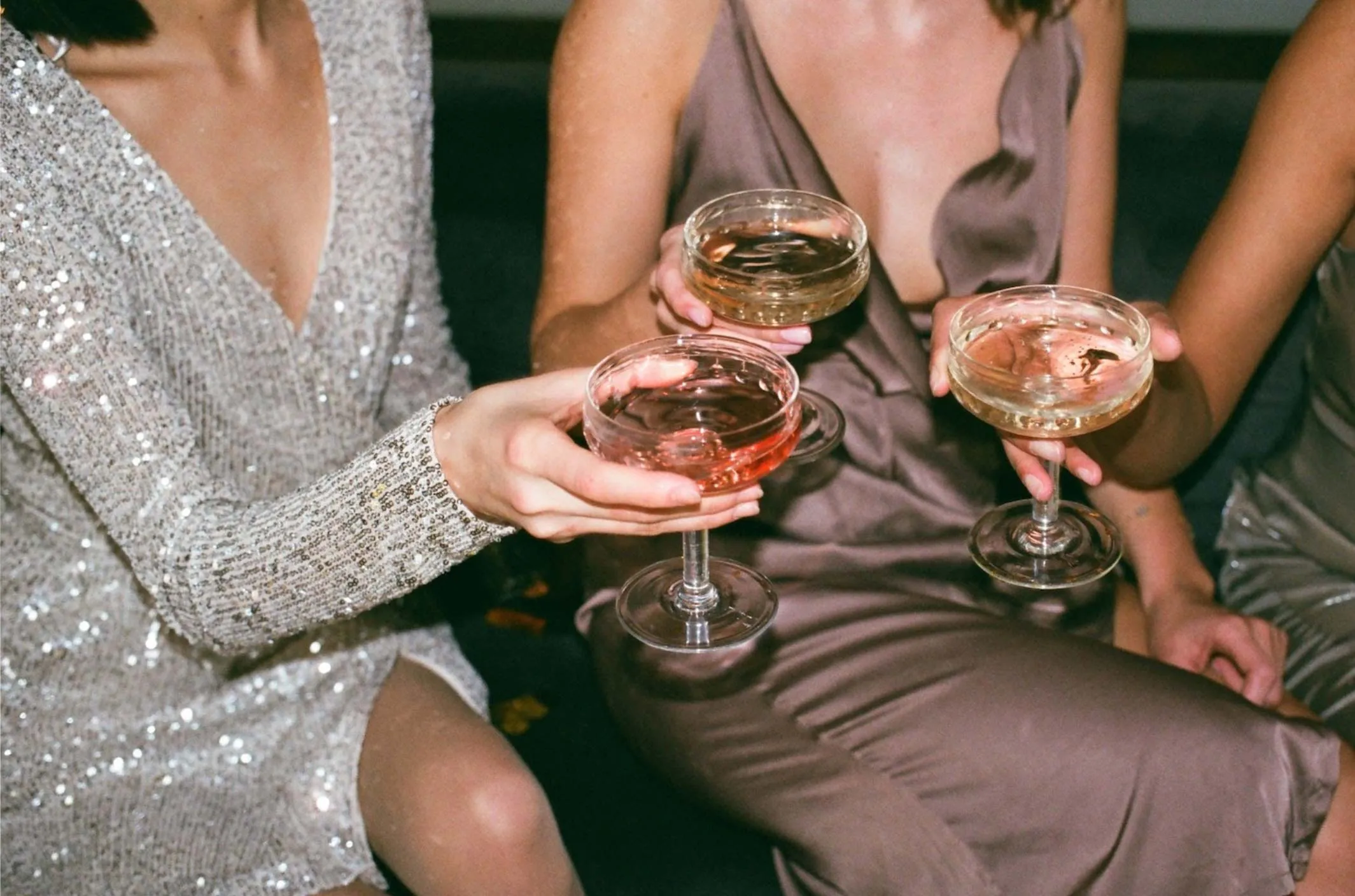 three women wearing cocktail dresses share a round of martinis