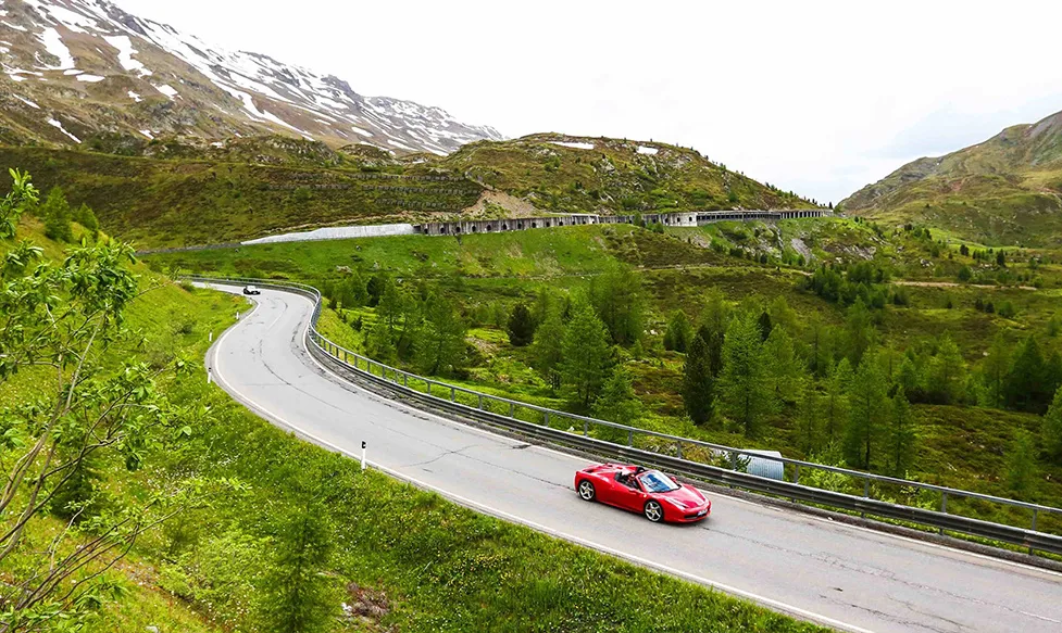 A red Ferrari 488 takes on a sweeping section of road in Italy’s snow-capped hills