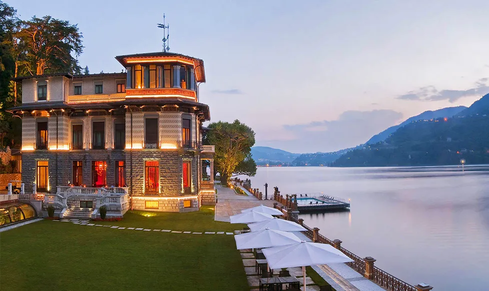 An exterior shot of the Mandarin Oriental at Lake Como shows the historic building elegantly lit as dusk draws in over the lake