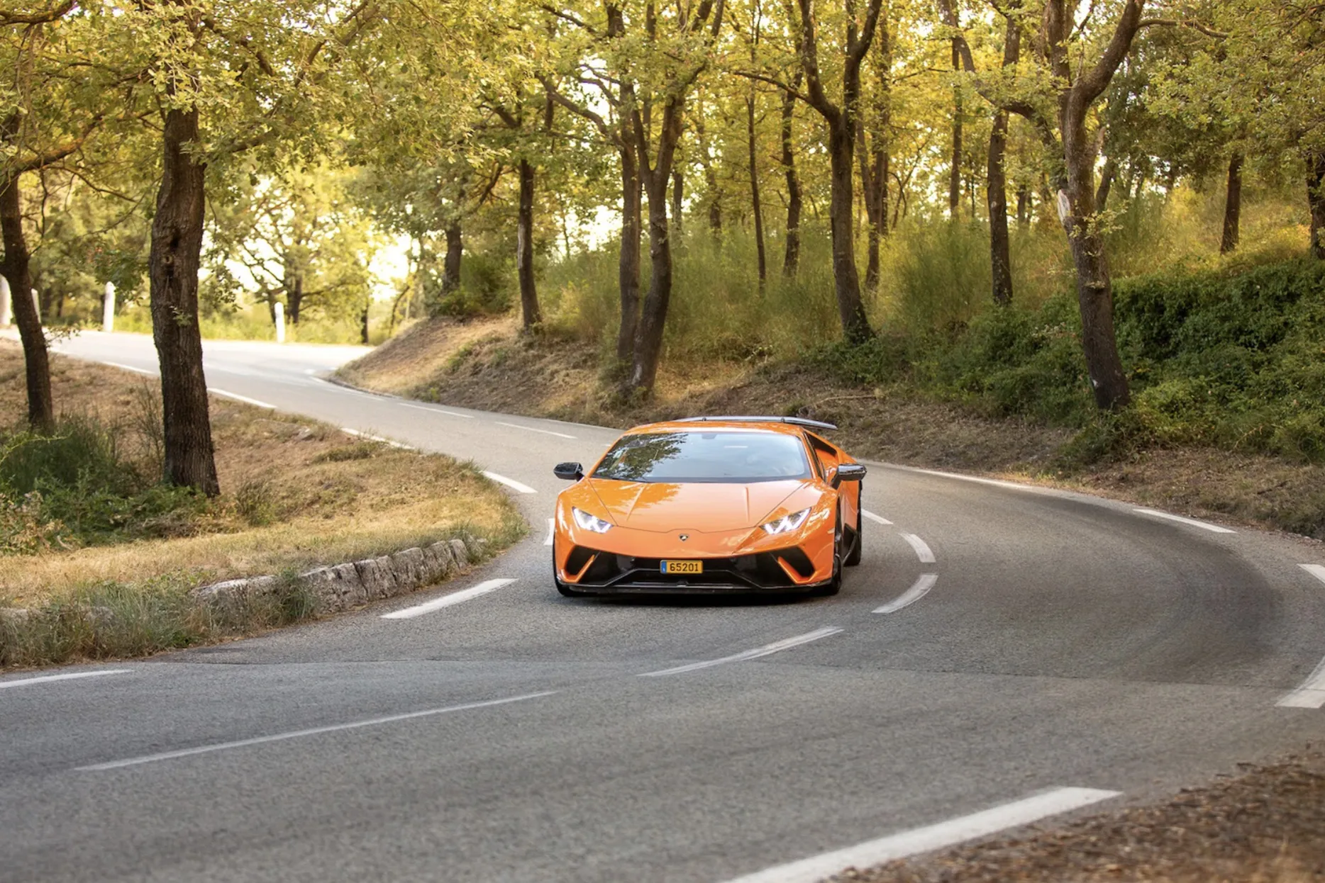 An orange Lamborghini makes its way through a forest in France