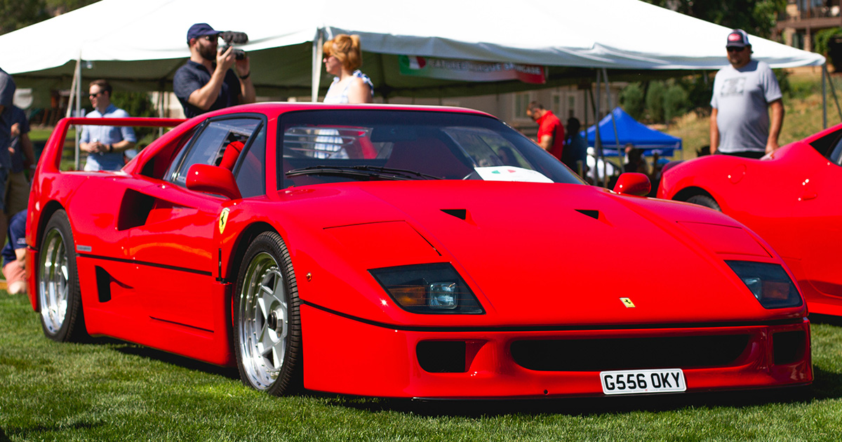 Red supercar sitting parked on a grass show ground surrounded by onlookers.