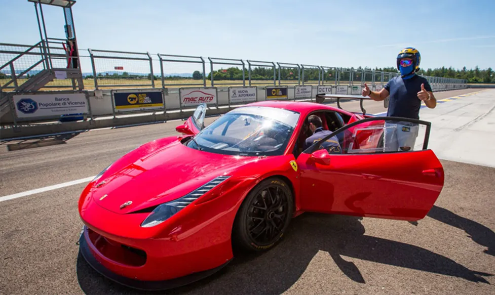 A track-ready red Ferrari is prepared to be driven round the Monza circuit by one of Ultimate Driving Tours' guests. He has two thumbs up.