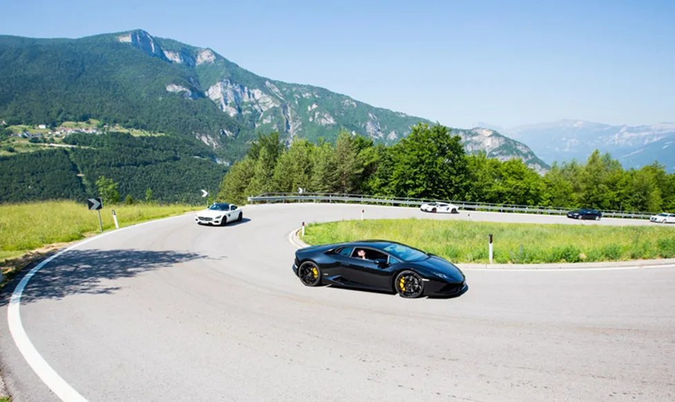 A black Lamborghini Huracan leads a troupe of supercars up a hill road Italy