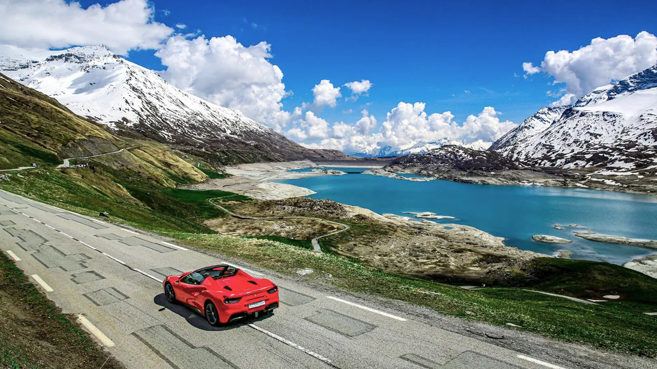 A red supercar driving alongside a lake and snow-capped peaks