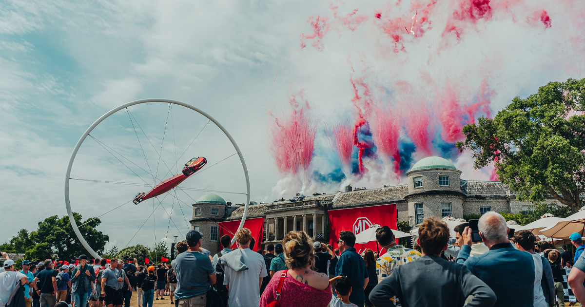 A huge sculpture with long beams with a racing car on each beam in front of Goodwood House
