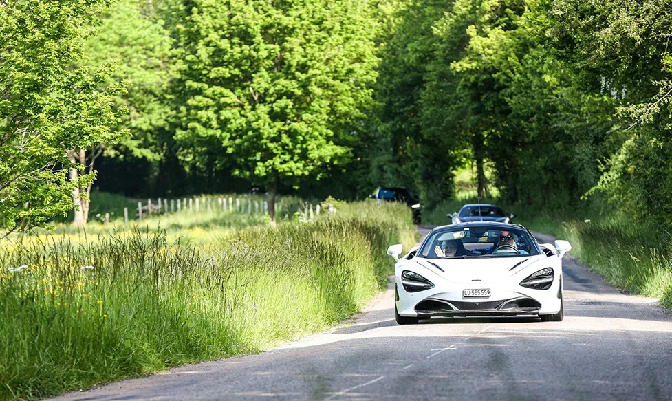 A white McLaren 720S being driven on a green country lane by guests of Ultimate Driving Tours