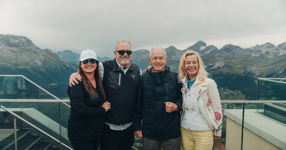 Two couples smile in front of a stunning mountain backdrop as part of a luxury driving tour