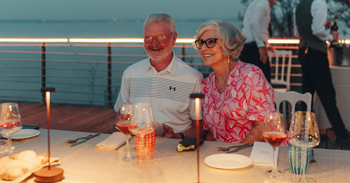 A happy elderly couple in smart casual dress enjoying an al fresco meal on a European tour.
