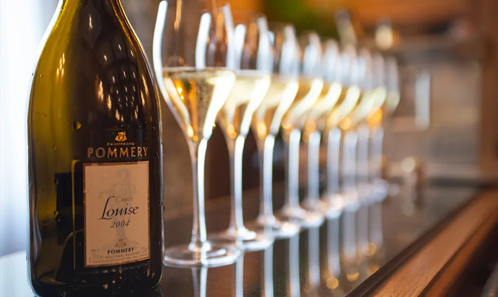 An empty bottle of Pommery Champagne sits next to a line of full champagne flute in France