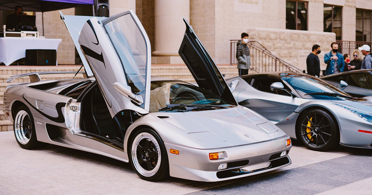 Silver supercar with open scissor doors sitting on a plaza.