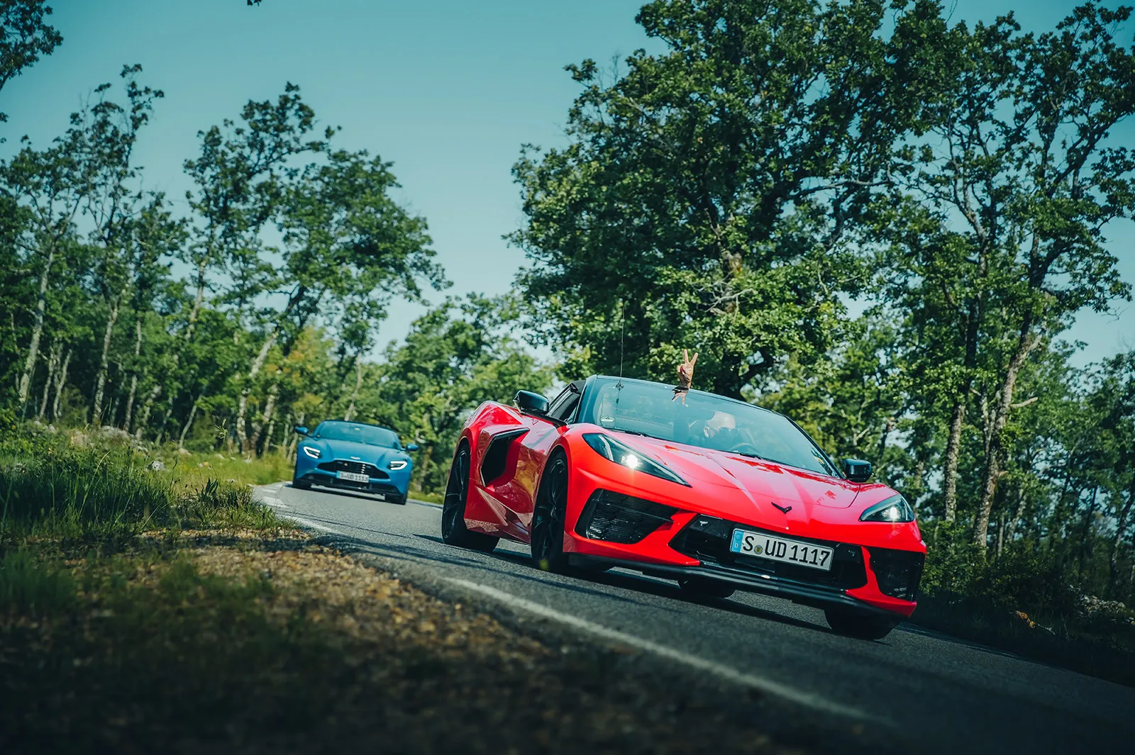 An Ultimate Driving Tours guest does the peace sign for the camera from their red Chevrolet Corvette on a forest road