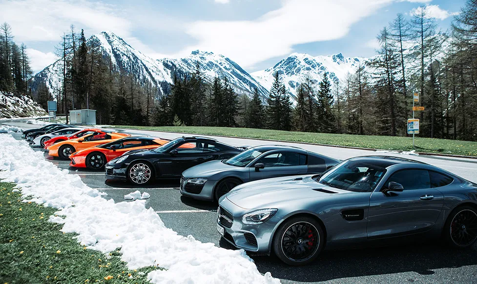A line of supercars sit in an alpine carpark on an Ultimate Driving Tours luxury holiday