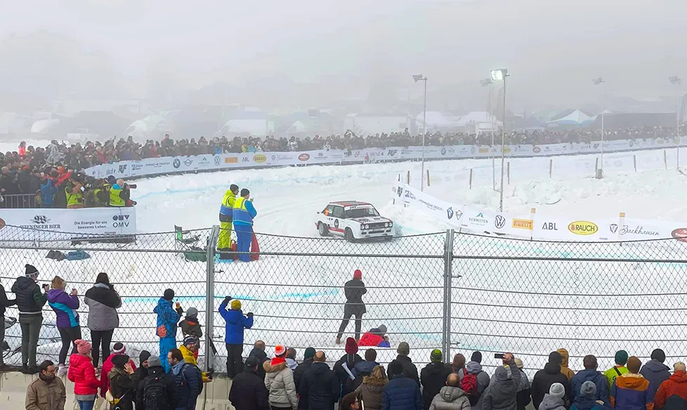 A rally car drifts around a corner on ice as a crowd watches on in Sweden